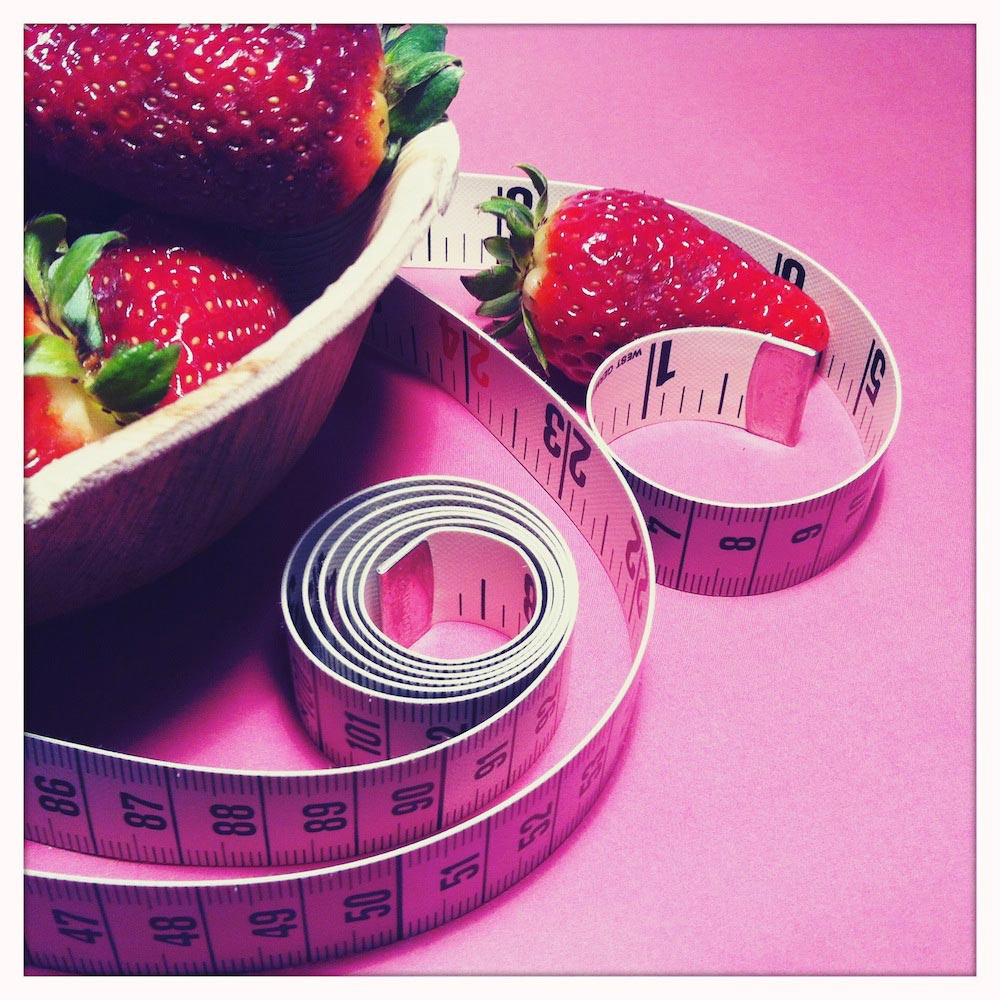 Ein Maßband und Erdbeeren auf einem pinken Tisch.